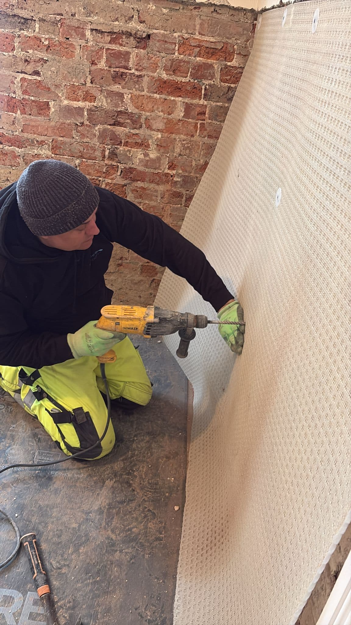 Brighton Damp Proofers fitter fixing a dimpled cavity drain membrane to a bare brick wall with sealed plugs